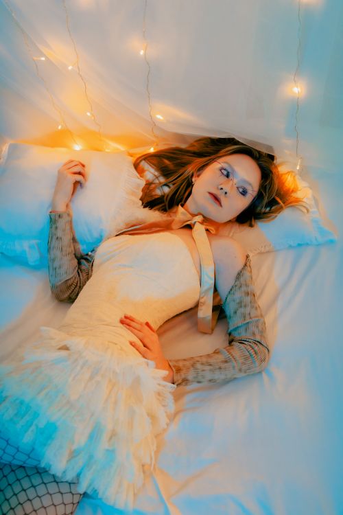 Free Woman in elegant dress lying on bed surrounded by warm string lights. Stock Photo