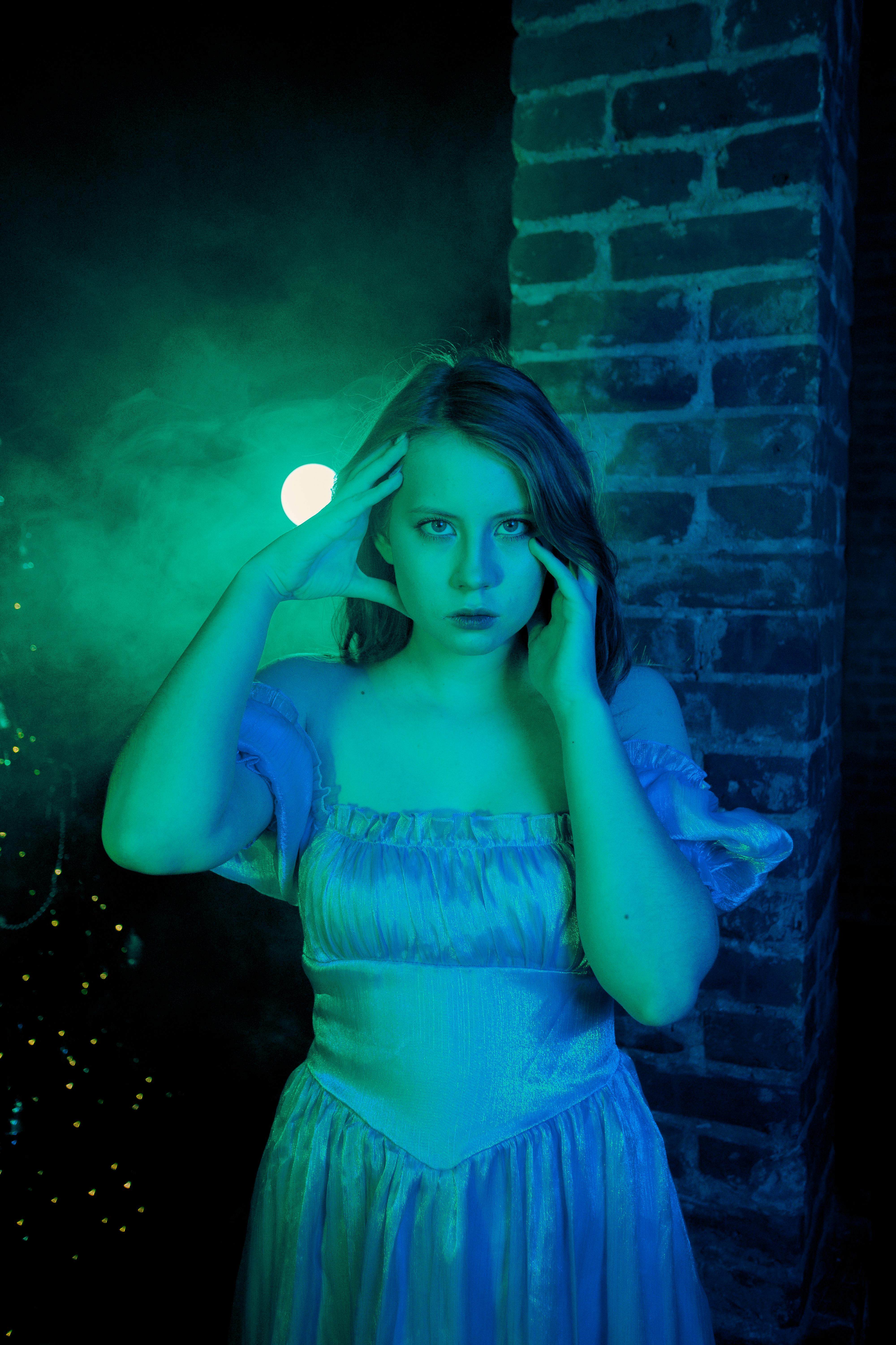 Kostnadsfria Mystiskt porträtt av en kvinna i blått ljus mot en tegelstensbakgrund, som skapar en fantasiatmosfär. Stock foto