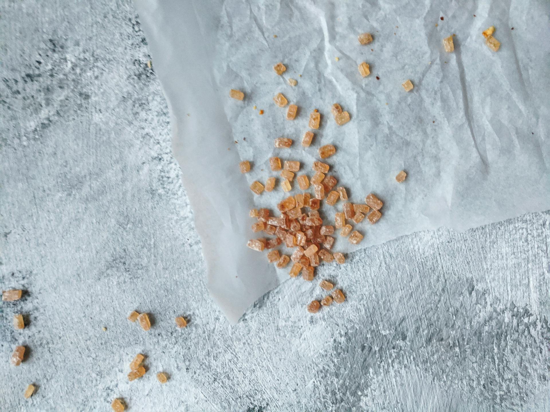 Close-up of coarse brown sugar scattered on parchment paper surface.