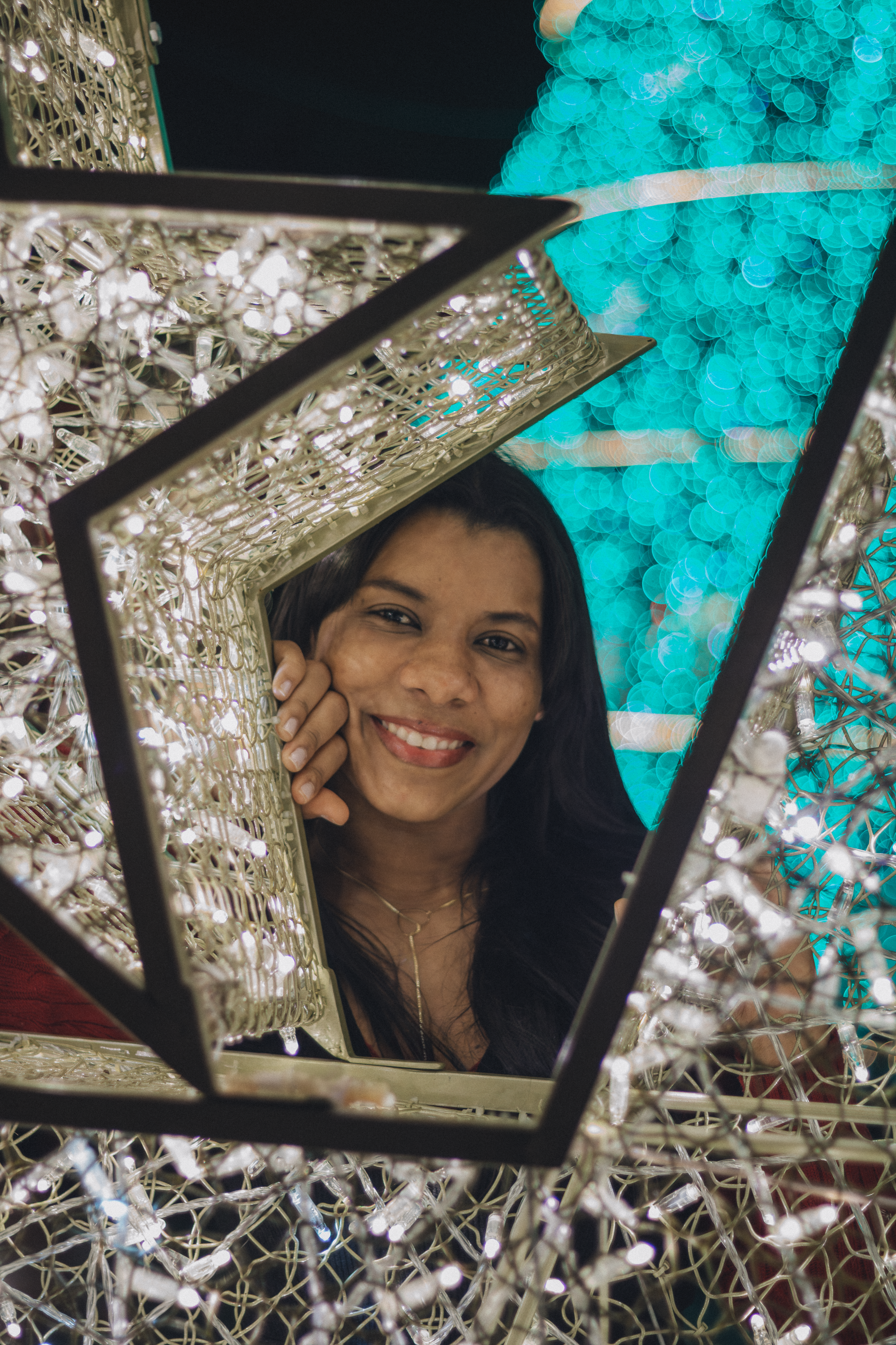 A woman smiles warmly through a decorative festive light frame.