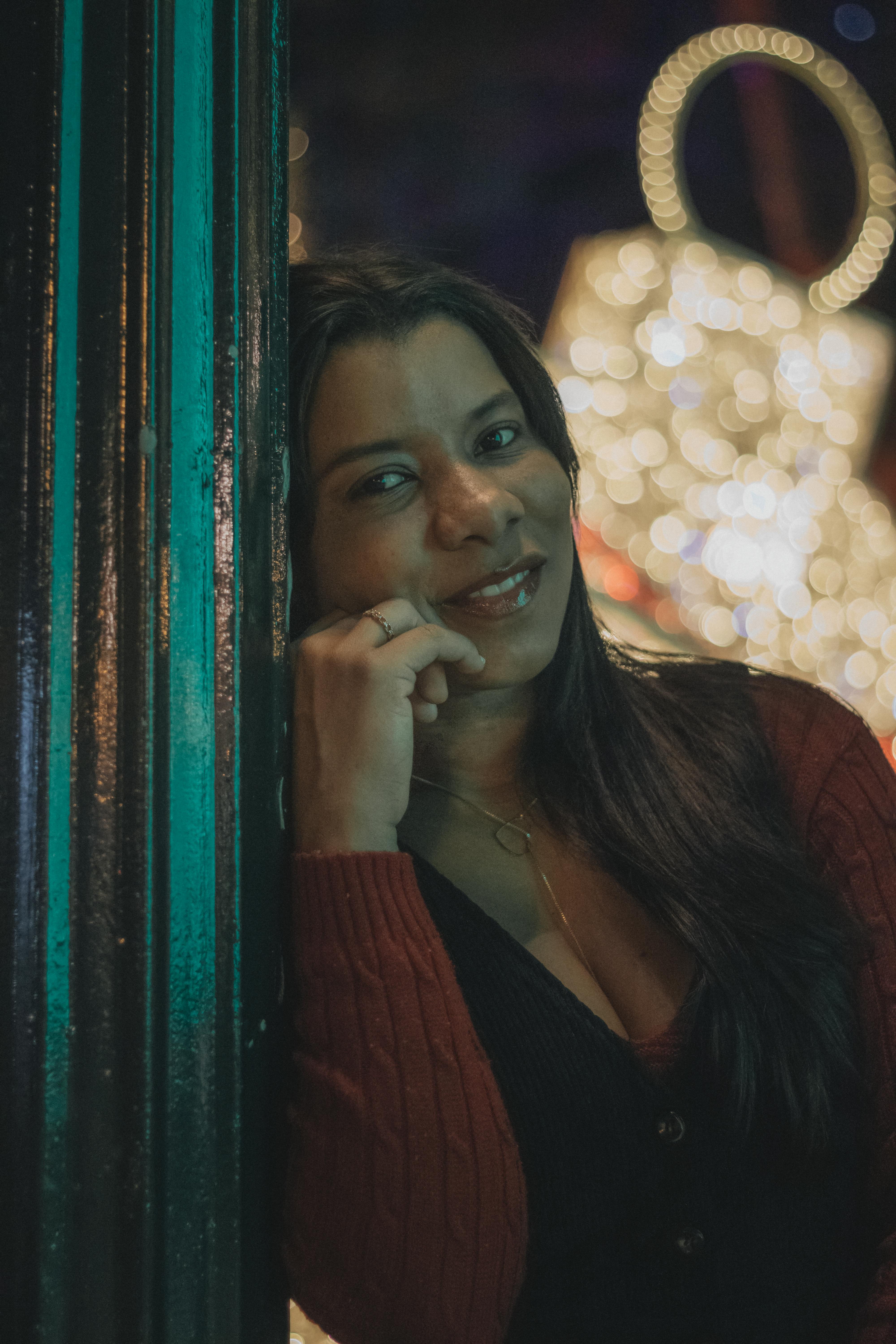 grátis Mulher sorrindo em frente a luzes festivas, criando uma cena calorosa e alegre. Foto profissional