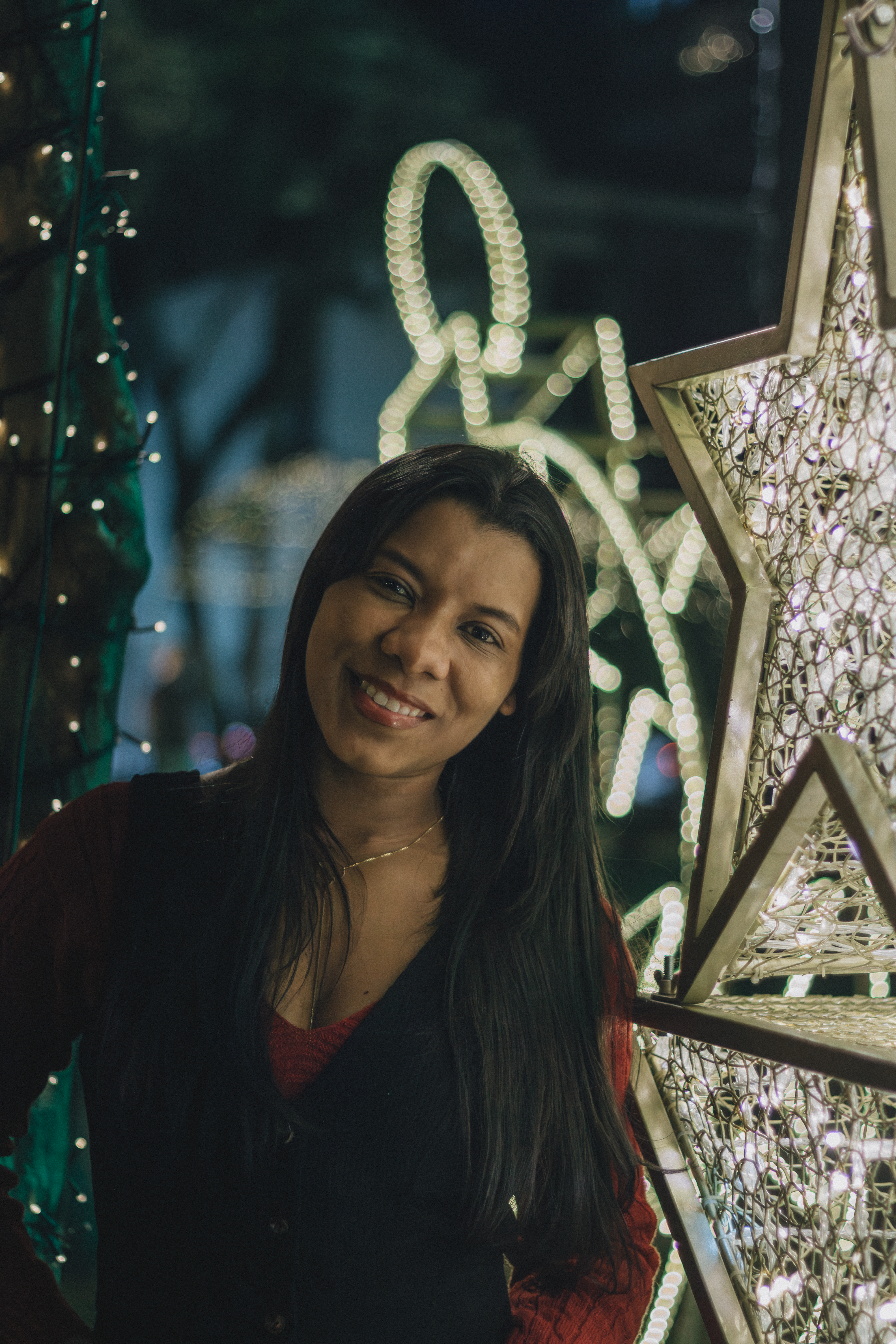 Woman smiling among illuminated Christmas decorations, embracing holiday spirit.