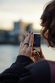A person photographing a city skyline with a handheld camera during sunset.