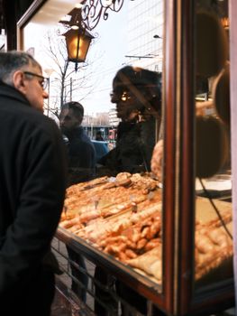 Shoppers gaze at delicious pastries through a bakery window, urban setting.