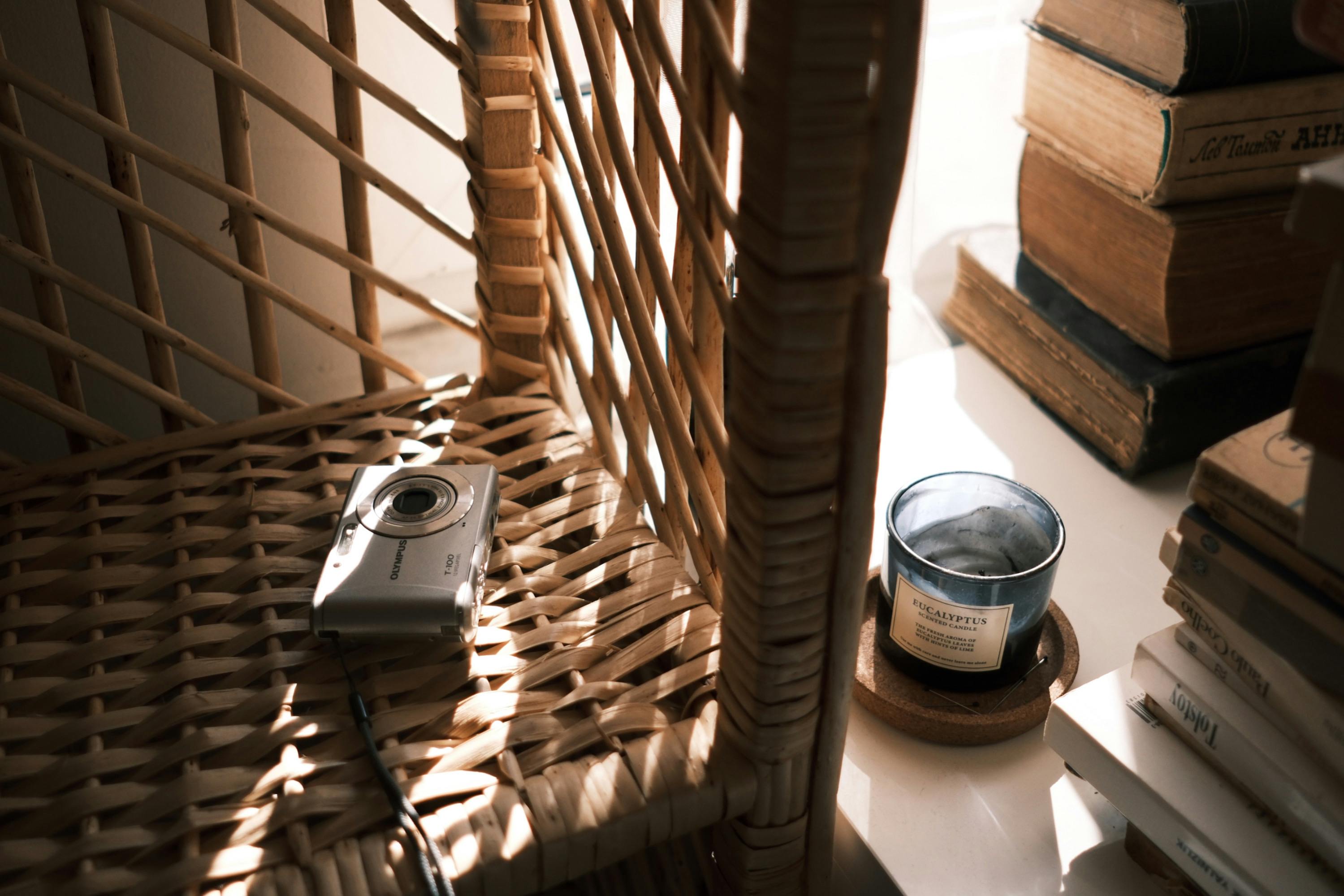 Gratuit Scaun din răchită scăldat în soare, cu un aparat foto vintage și cărți, pentru o atmosferă confortabilă și nostalgică. Fotografie de stoc