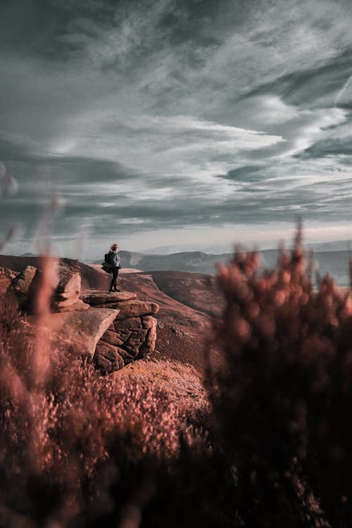 Person Standing on Cliff Under Cloudy Sky