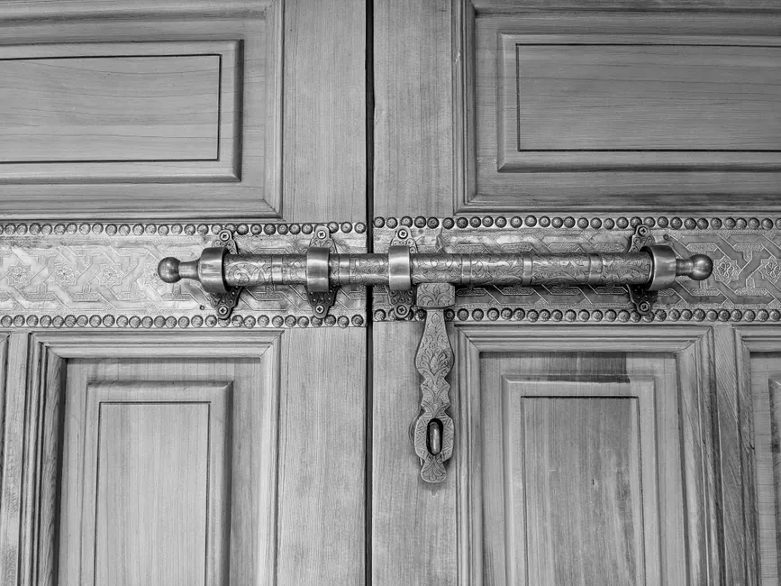 Long verrou en métal ouvragé posé en travers d'une porte ancienne à double vantail, photo en noir et blanc