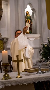 A priest conducts a Holy Communion ceremony in a church altar setting with religious icons.