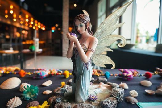 A delicate fairy figurine with wings surrounded by seashells and vibrant decorations on a café table.