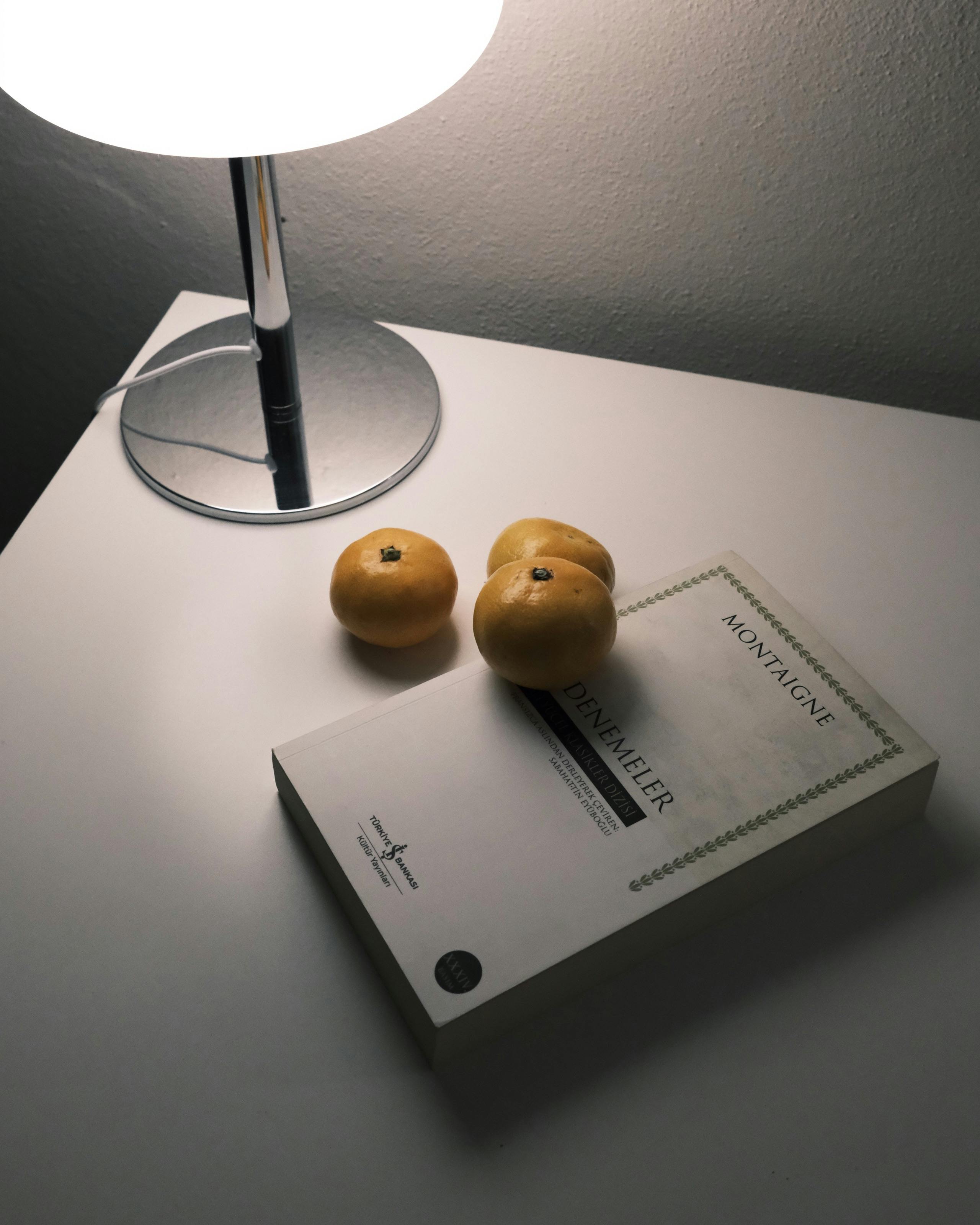 Kostenlos Zitronen und ein Buch auf einem minimalistischen Schreibtisch im warmen Licht einer Lampe. Stock-Foto