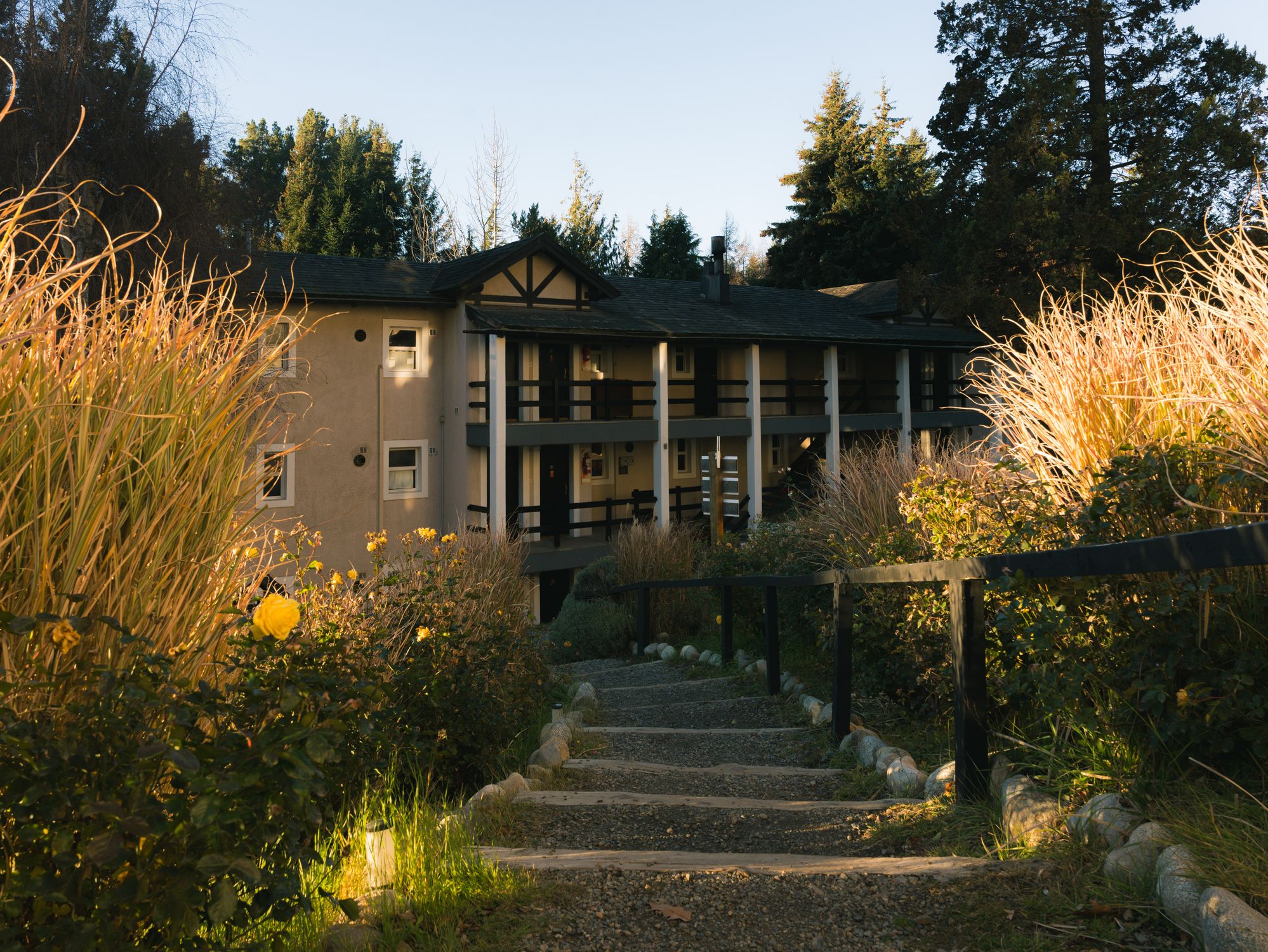 A rustic lodge framed by a lush garden pathway in warm golden sunlight, creating a serene atmosphere.