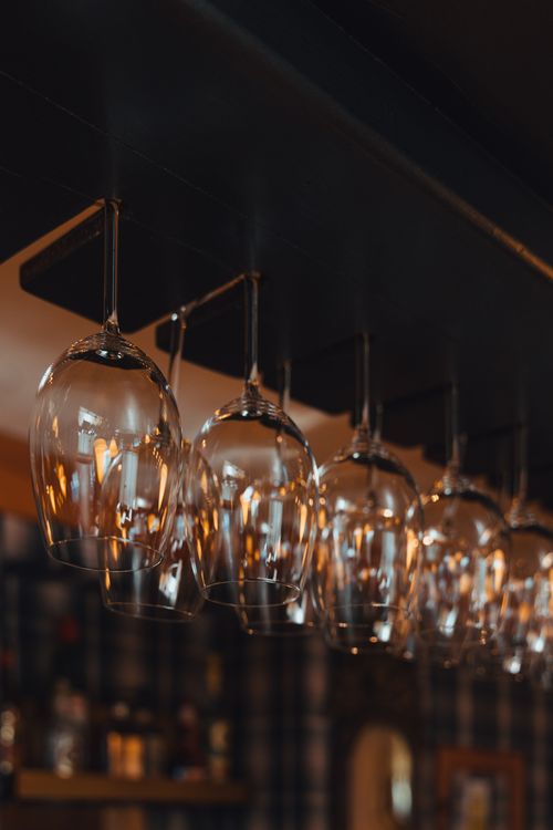 Free Row of elegant glass wine globes hanging upside down with warm lighting, creating a cozy bar ambiance. Stock Photo