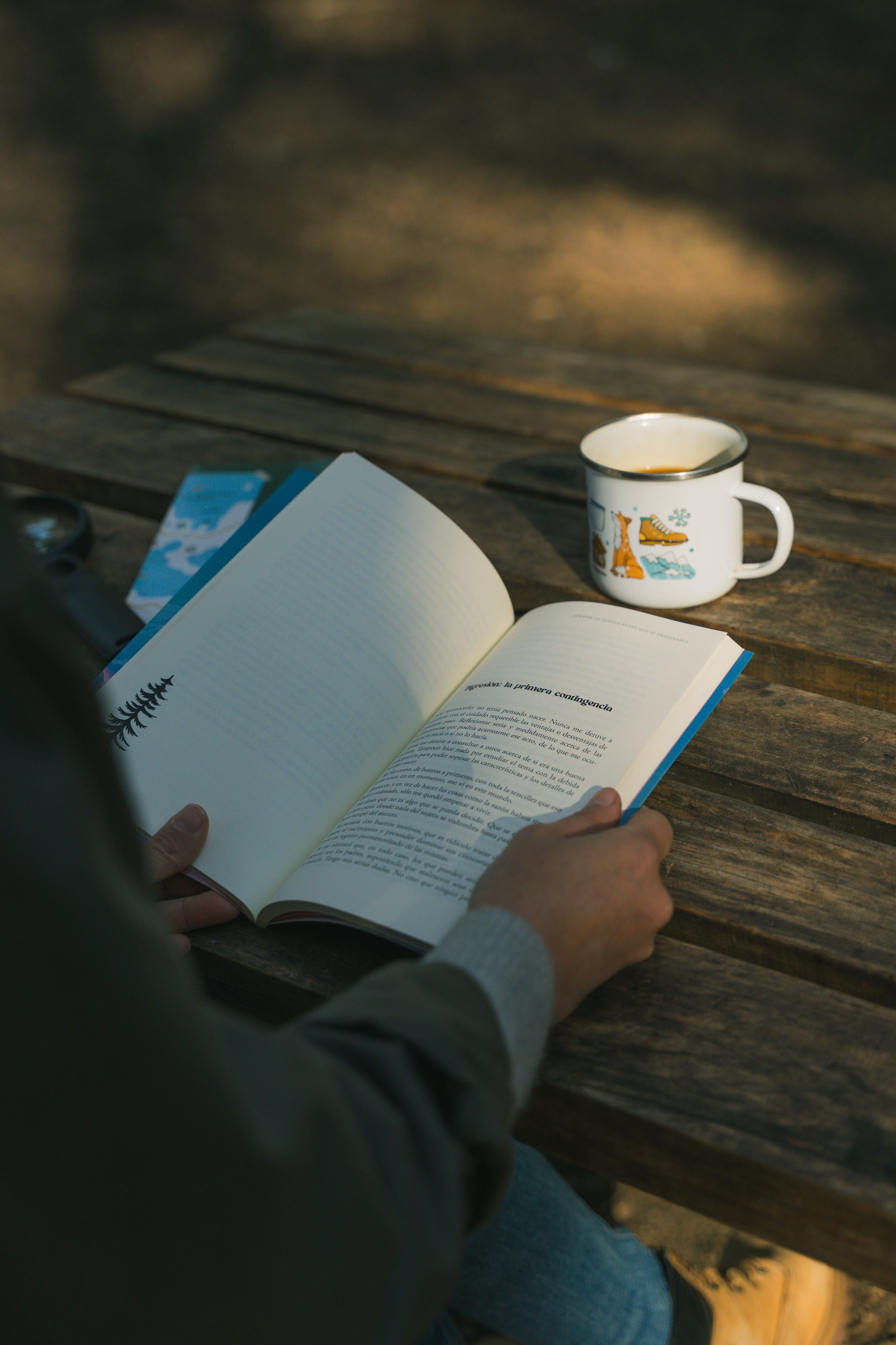 A person enjoying a book with coffee on a wooden table in natural sunlight.