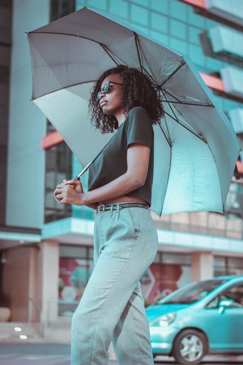 Free Fashionable woman standing with umbrella on an urban street, embodying modern style. Stock Photo