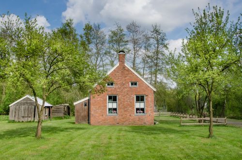 Free A small rustic brick barn surrounded by green trees and grass, under a clear summer sky. Stock Photo