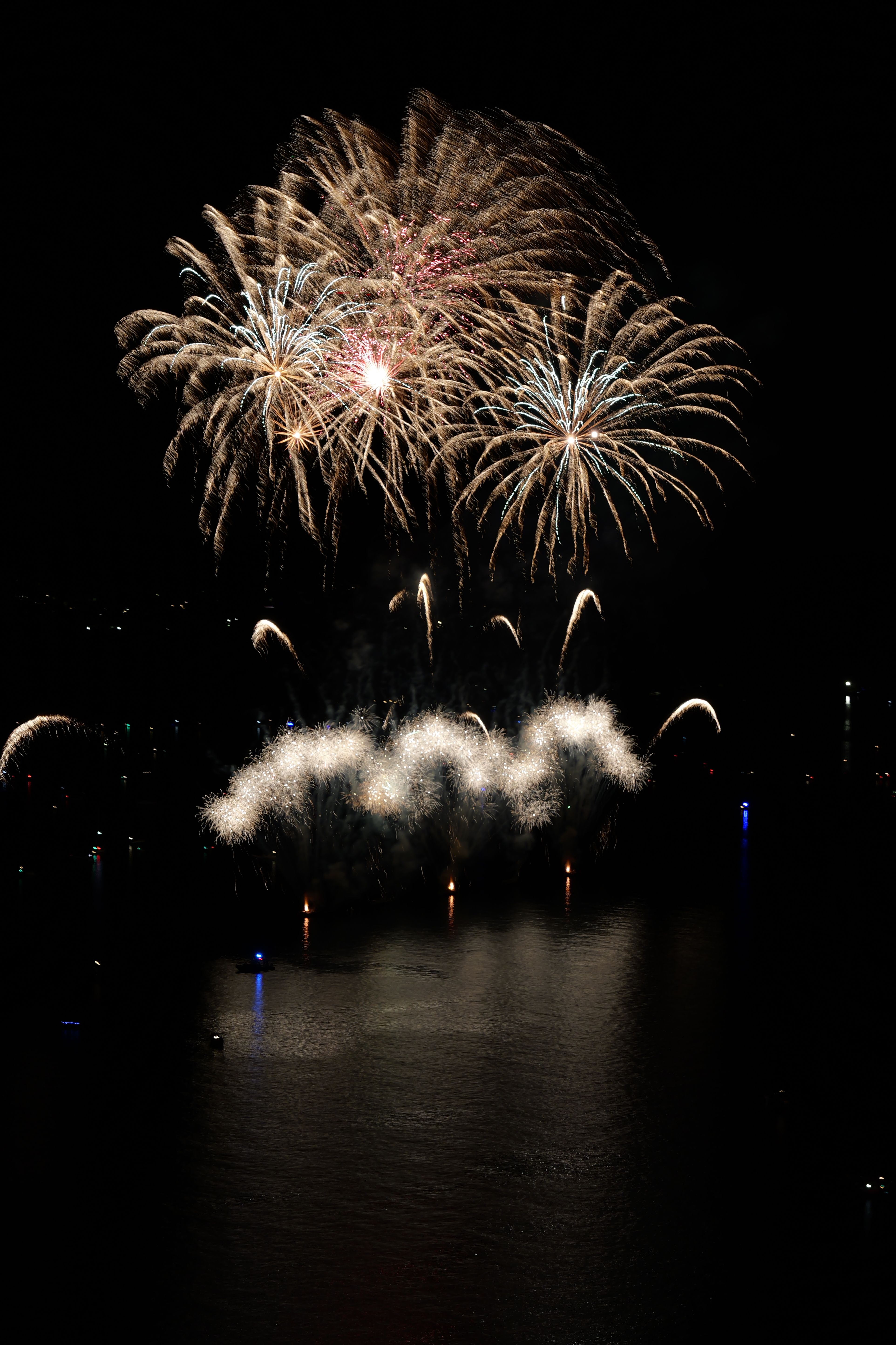 Vibrant fireworks illuminate the night sky over a calm water surface creating mesmerizing reflections.