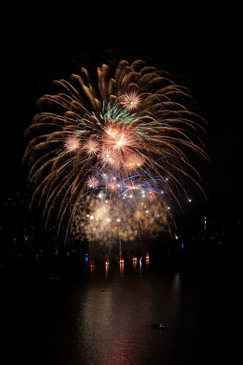 Free Colorful fireworks explode over a city waterfront at night, creating vibrant reflections in the water. Stock Photo