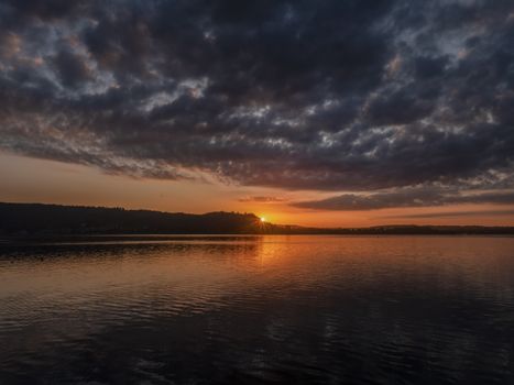 A breathtaking sunset view with dramatic clouds over a serene lake.