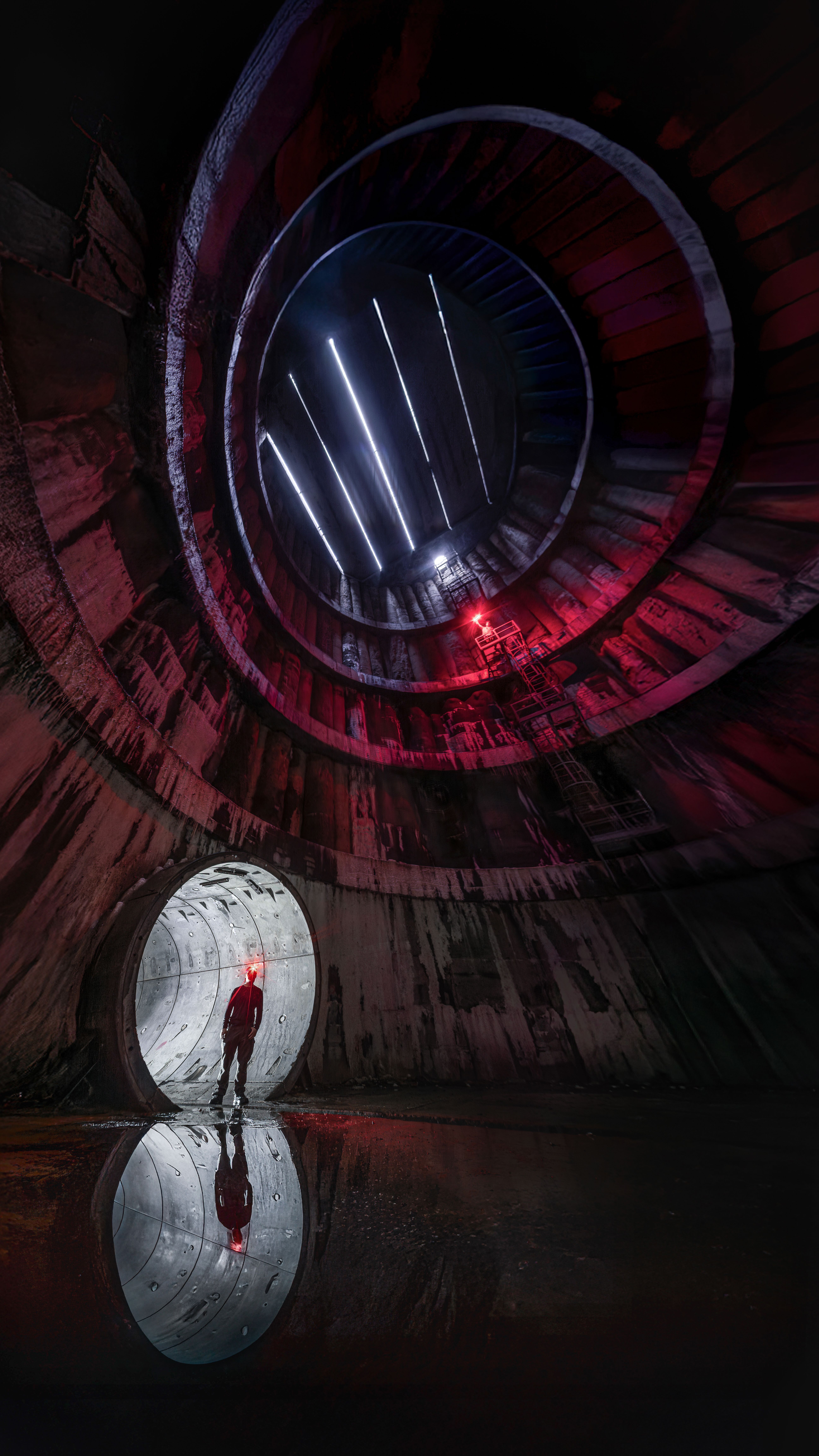 A person stands in a futuristic tunnel with reflective water and neon lighting creating a dramatic atmosphere.