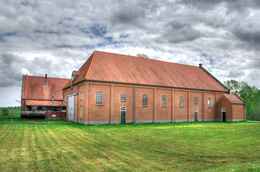 Red brick barn on a sunny day with lush green grass, ideal for rural scenery.