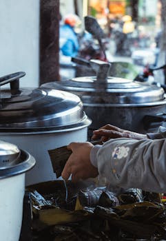 A street vendor is preparing traditional food with large steaming pots outdoors.