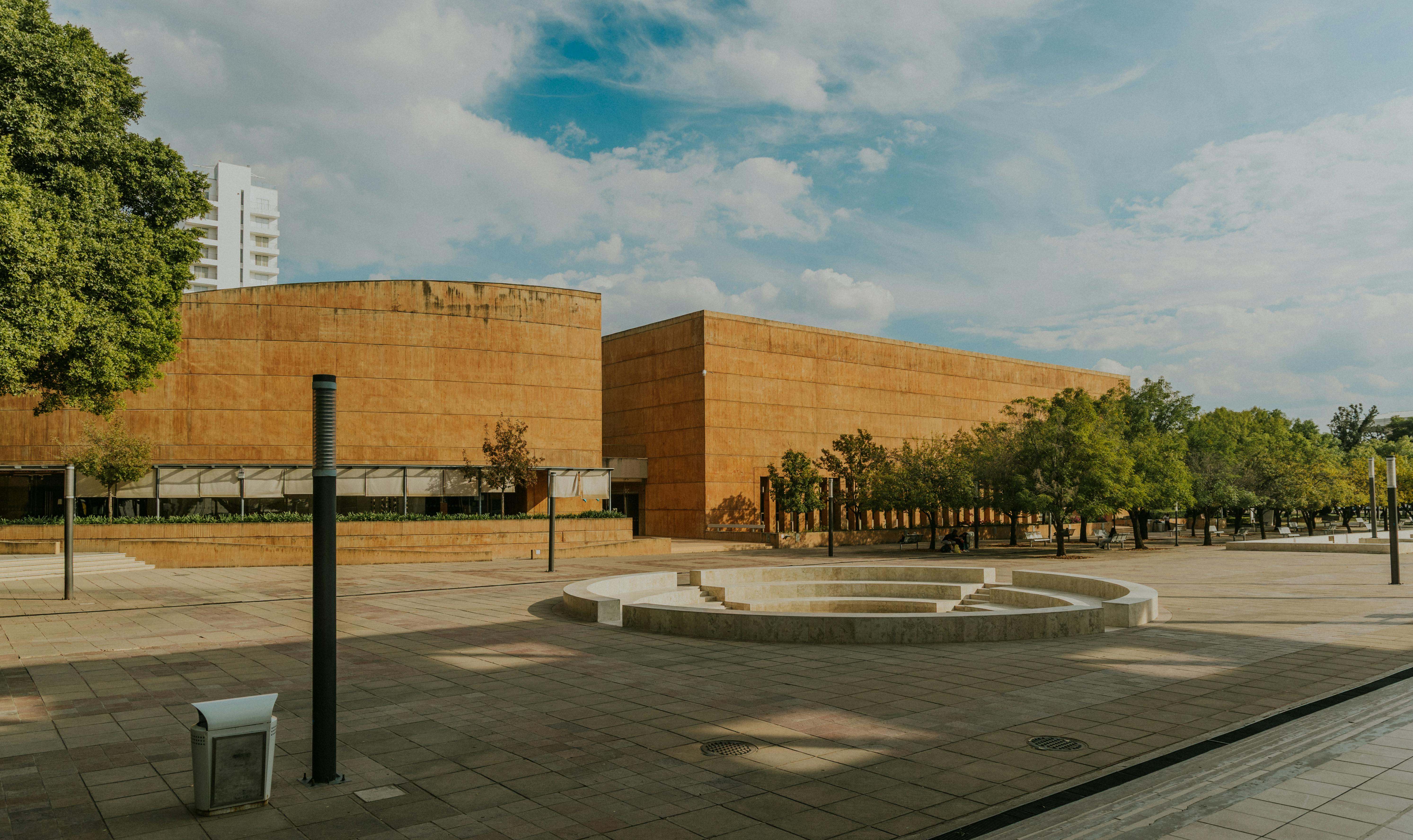 Ücretsiz Mavi gökyüzü altında modern bir bina ve açık bir meydanın yer aldığı kentsel mimari manzara. Stok Fotoğraflar