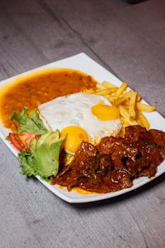 A savory dish featuring eggs, steak, fries, avocado, and salad on a white plate.