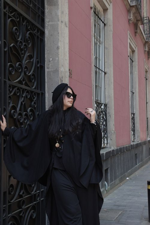 Free Stylish woman in gothic black attire leans on ornate gate next to historic building in Mexico City. Stock Photo