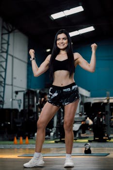 A woman confidently posing in a modern gym, showcasing fitness and strength.