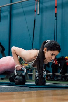 Athletic woman doing kettlebell push-ups in a gym setting, focusing on strength and fitness.