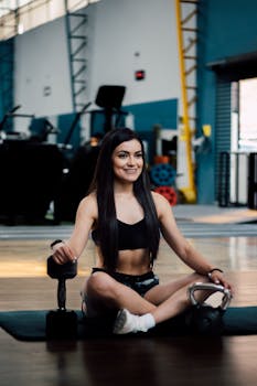 Smiling woman in gym attire seated with weights, embodying a healthy lifestyle.