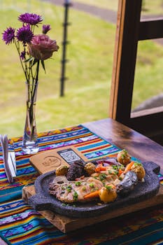 A traditional Peruvian dish served on a vibrant table with a flower vase by the window.