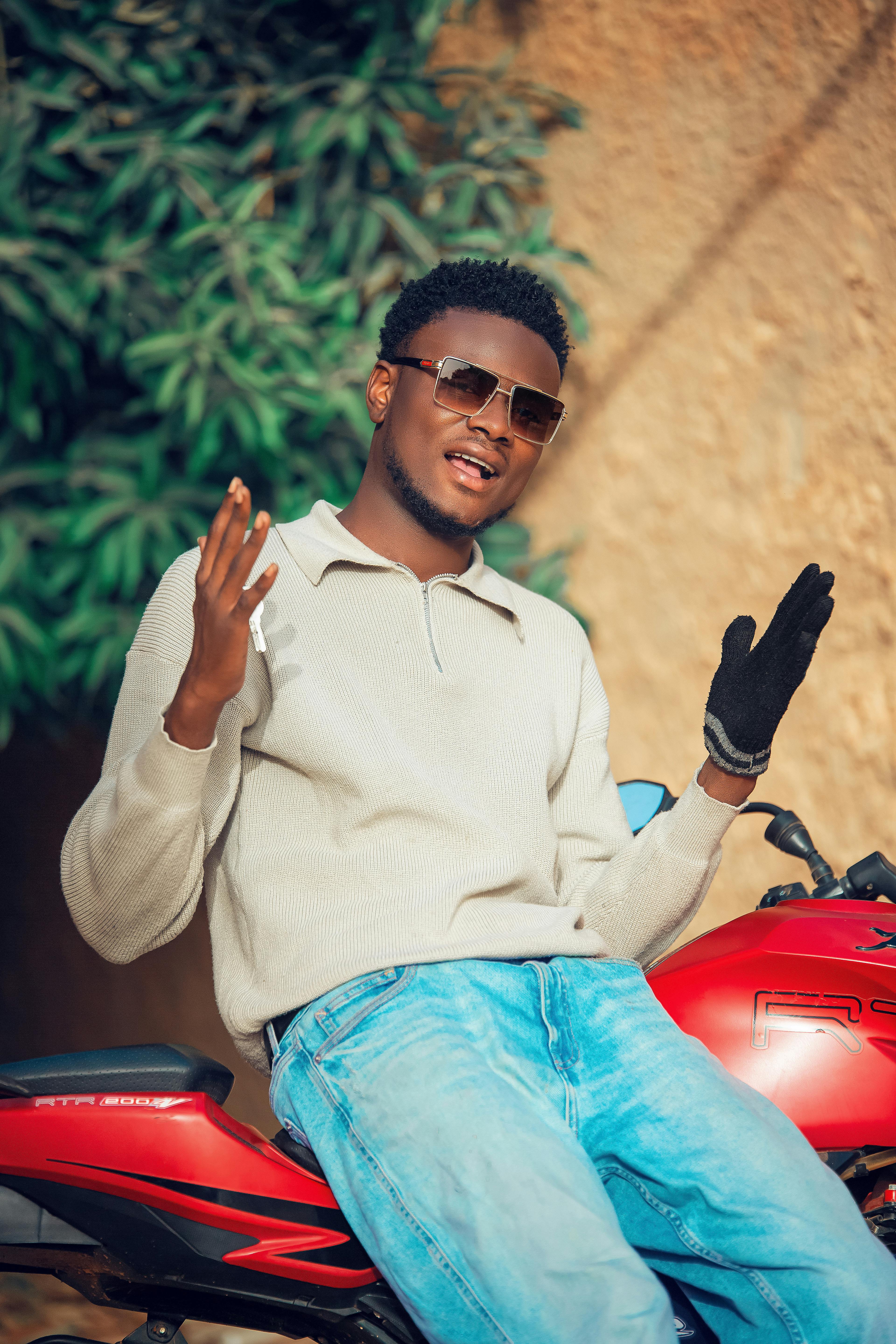Stylish young man wearing sunglasses posing confidently on a red motorcycle outdoors.