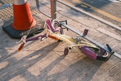 Free A child's purple bicycle laying on a city sidewalk next to a traffic cone in daylight. Stock Photo