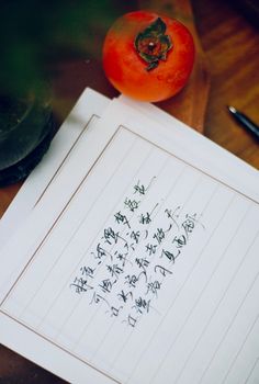 Handwritten Chinese poem beside a ripe persimmon on a wooden table.