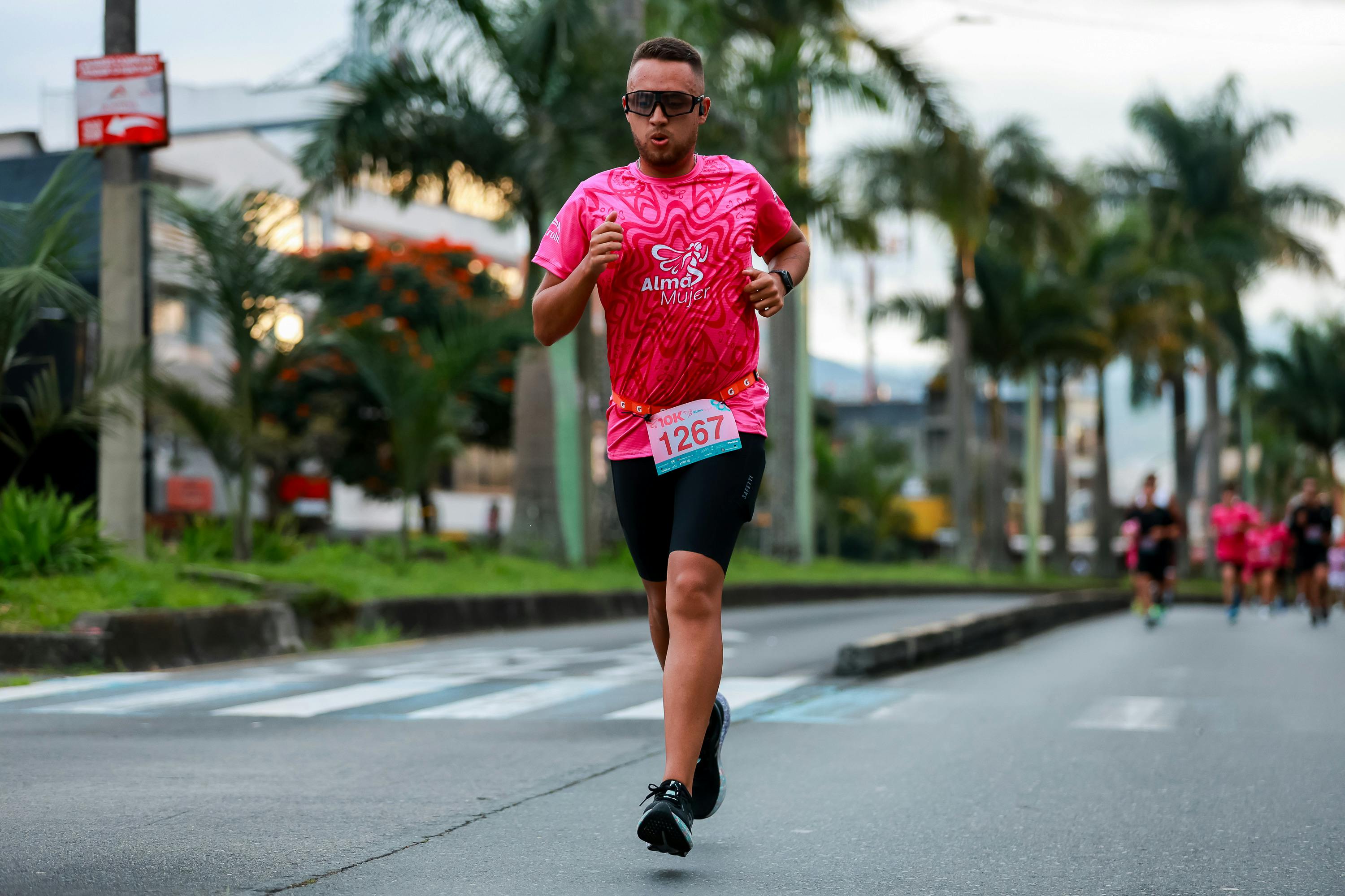 Focused athlete in sunglasses running a marathon race in tropical urban area.