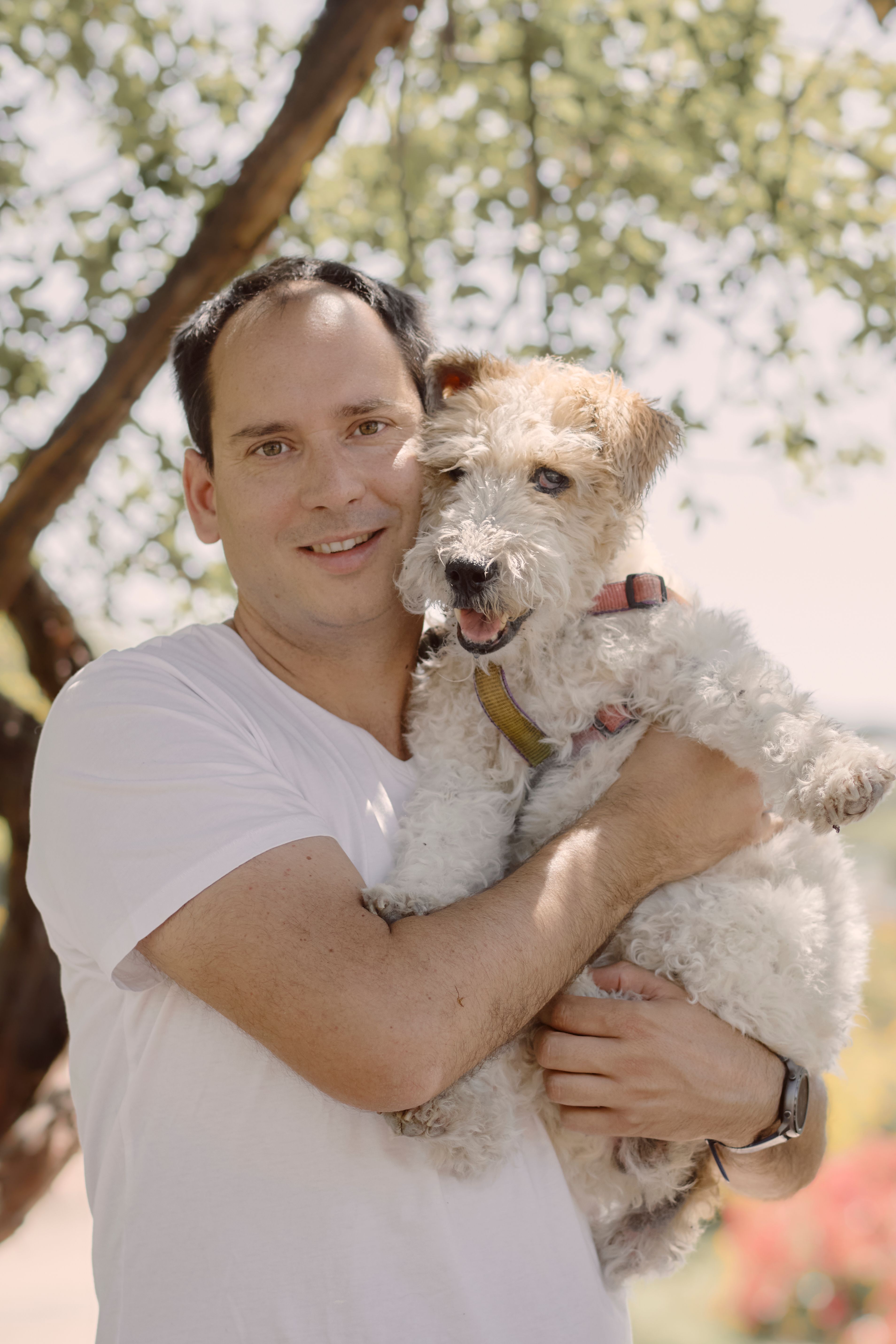 A man joyfully holds his Wire Fox Terrier outdoors on a sunny day.