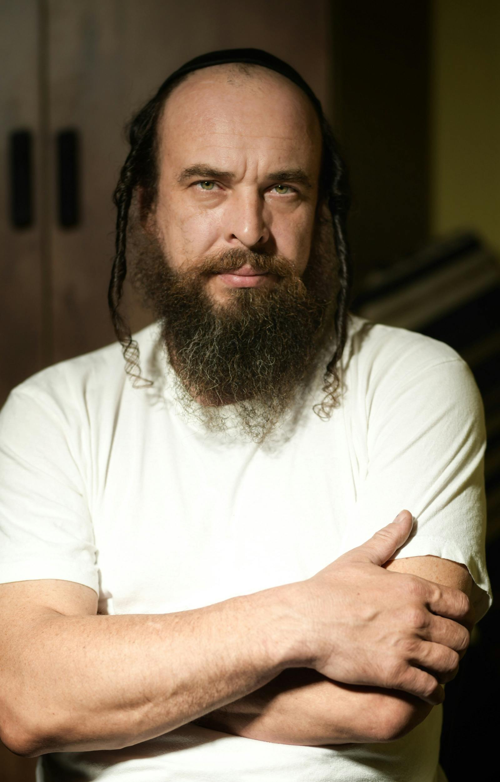 Portrait of a contemplative bearded man with crossed arms, indoors lighting.