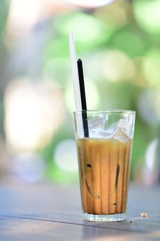 A glass of iced coffee with straws on a wooden table, bathed in sunlight.
