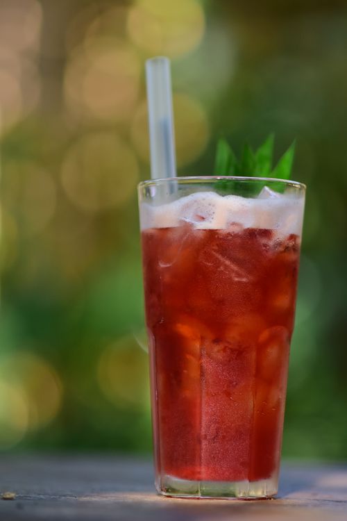 Free A tall glass of iced berry drink with mint leaves on a blurred outdoor background. Stock Photo