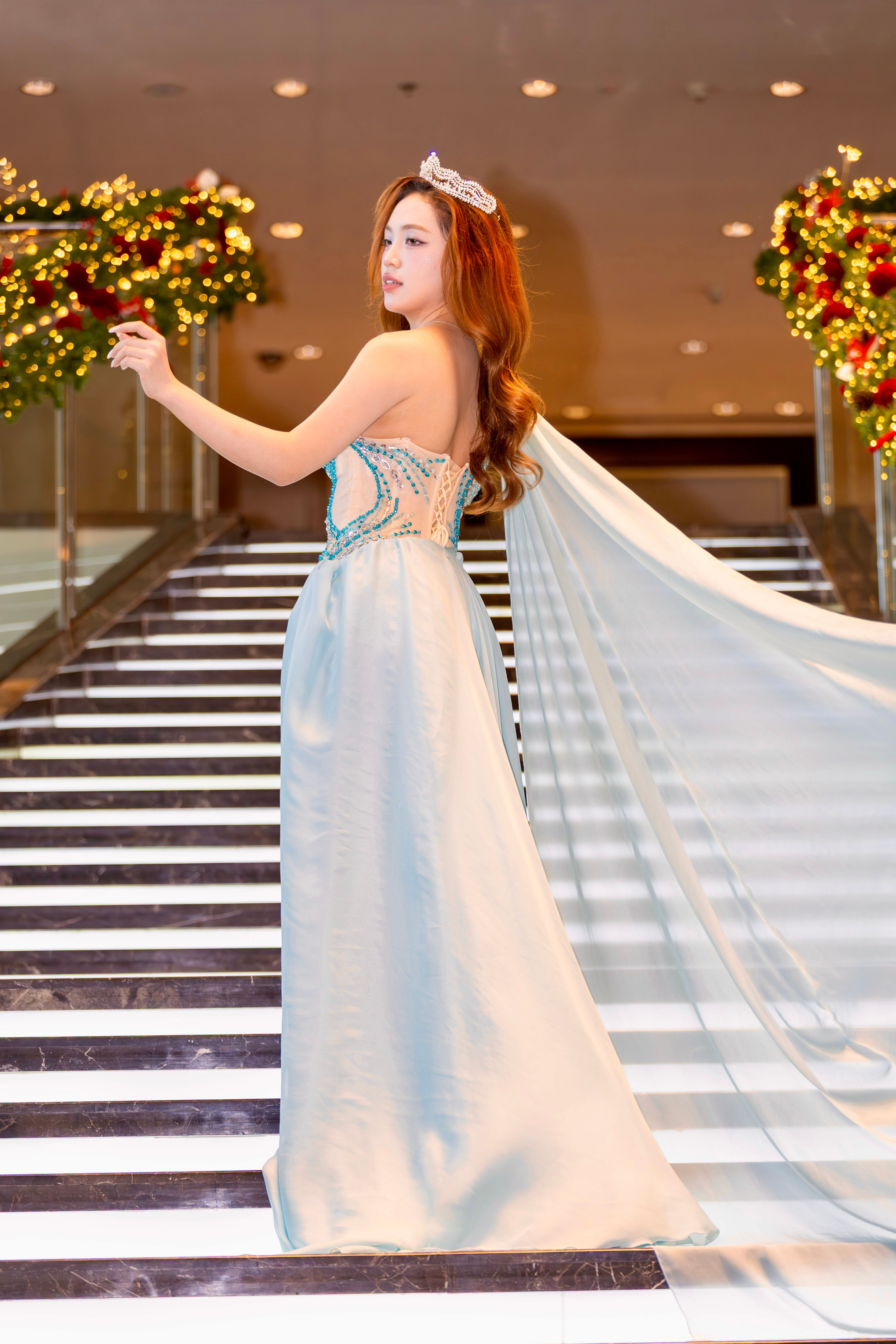Woman in evening gown and tiara poses on festive staircase in Hanoi.