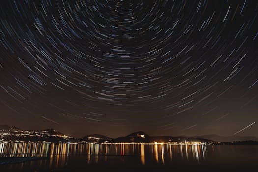A mesmerizing long-exposure photo capturing star trails above a serene lakefront at night.