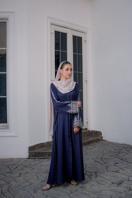 Portrait of a woman in a blue modest dress standing outside a white building.