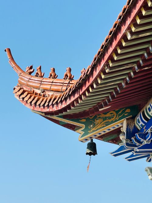 Free A decorative traditional Chinese temple roof with ornate figures against a clear blue sky. Stock Photo