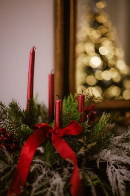 Free Elegant Christmas candles with red ribbon, evergreen, berries, and blurred tree lights. Stock Photo