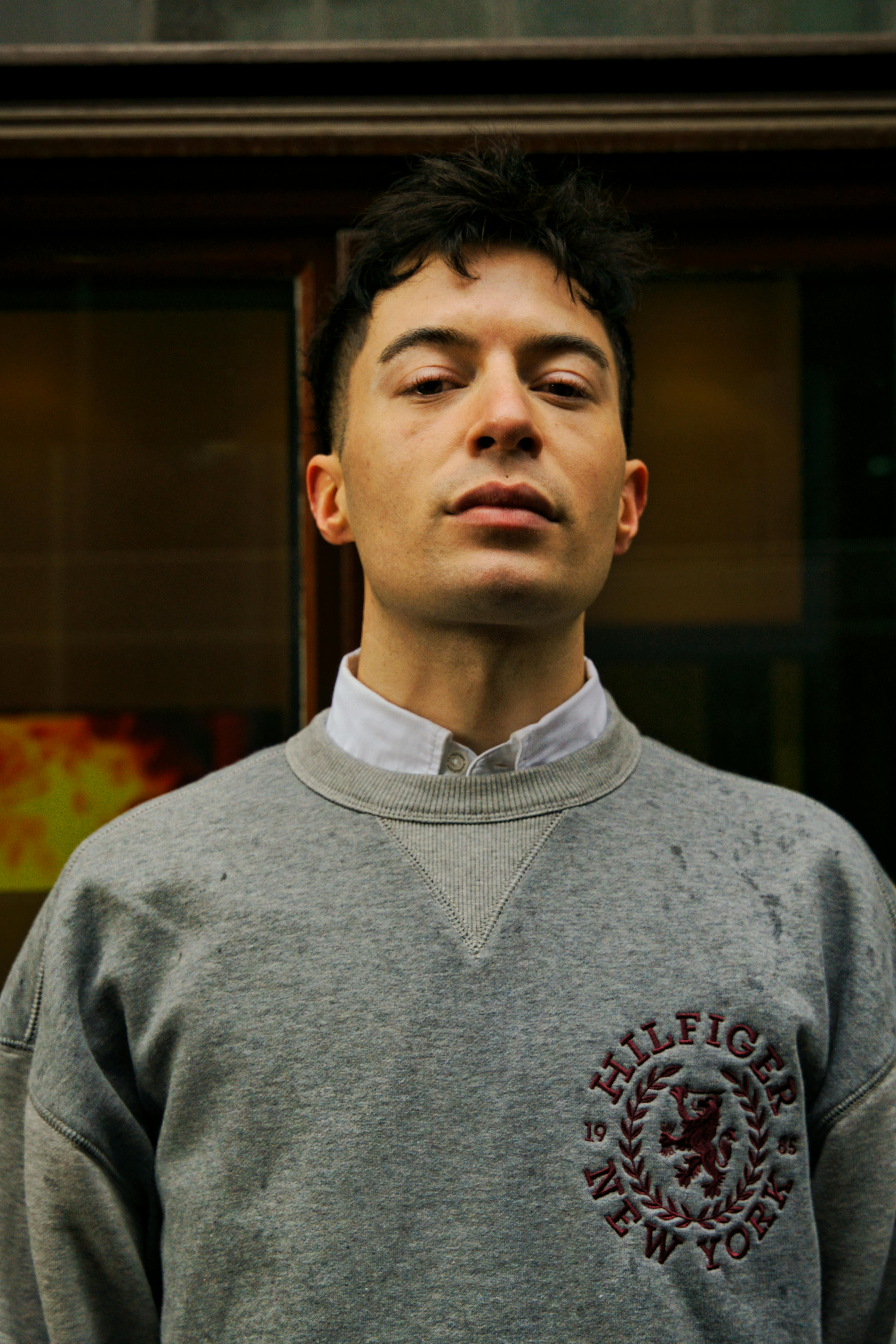 Close-up portrait of a man in a gray sweatshirt standing outdoors, evoking a modern lifestyle vibe.