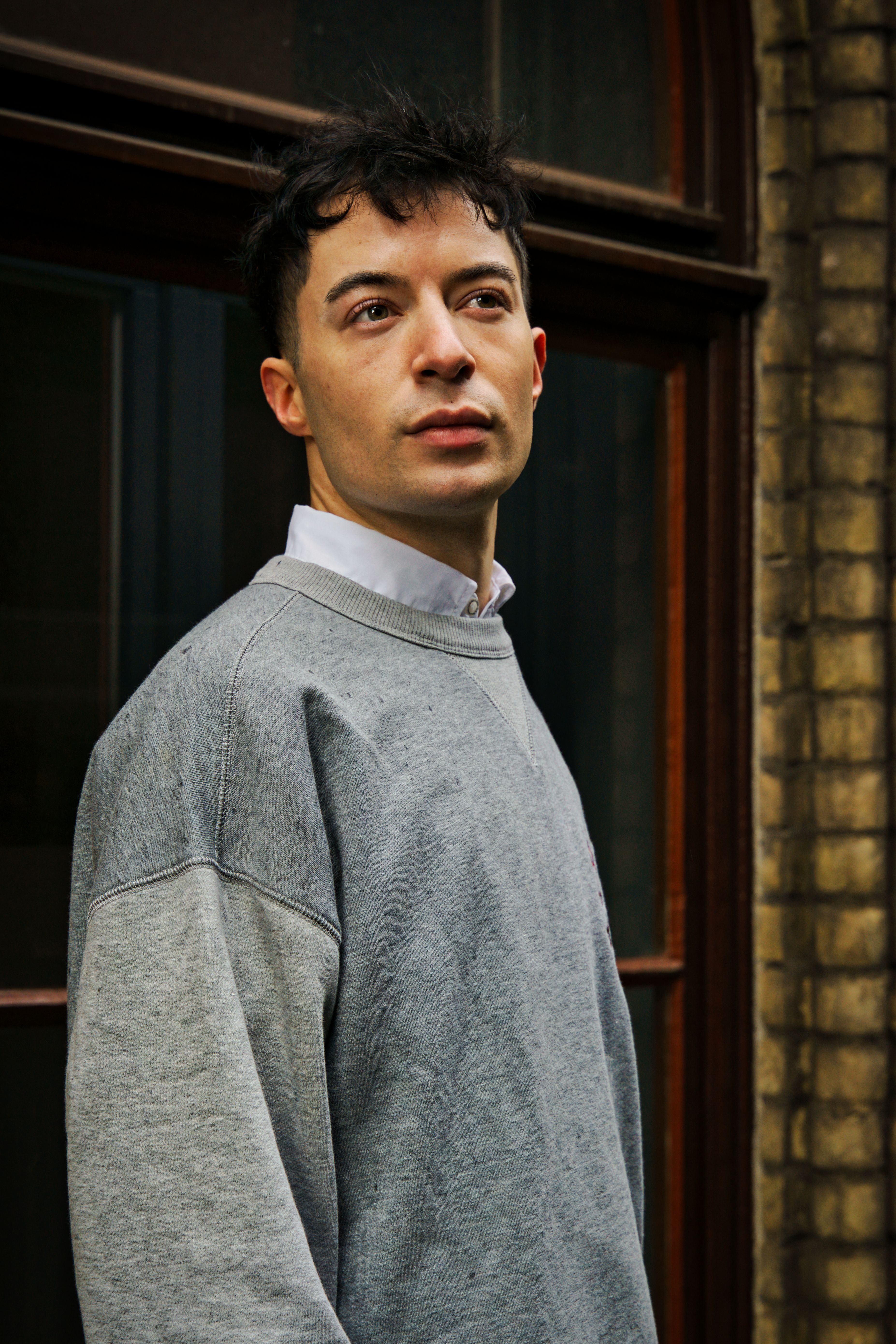 A young man standing outdoors in Bremen, wearing a grey sweater.