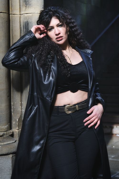 Free Confident woman posing in black outfit against a stone pillar, exuding a bold fashion statement. Stock Photo