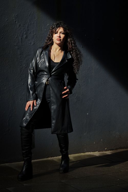 Free A woman in a black leather coat exudes confidence against a dark background. Stock Photo