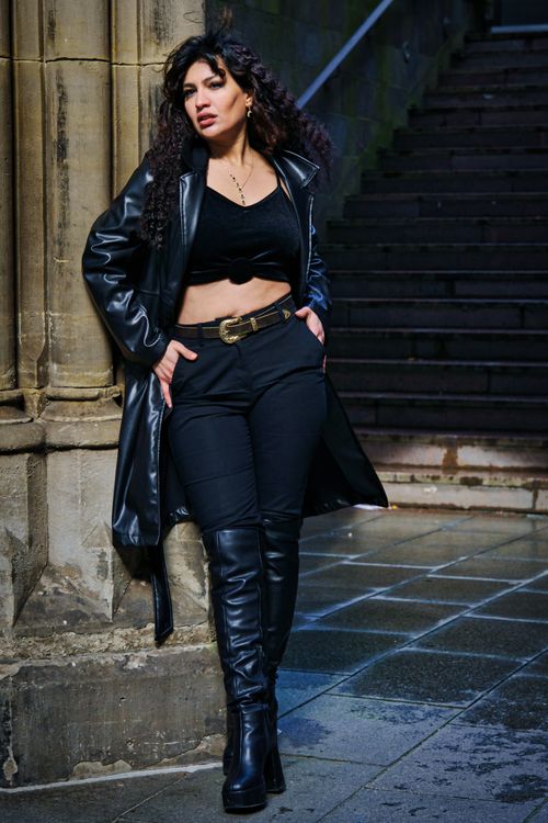 Free Chic woman in black outfit posing against historic stone wall in Bremen outdoor setting. Stock Photo